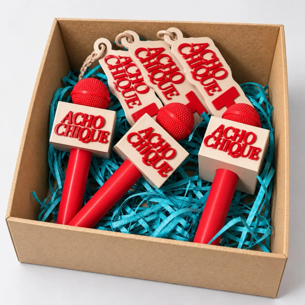 Chaveiros em forma de microfone vermelho com a marca Acho Chique, numa caixa kraft com papel picado azul