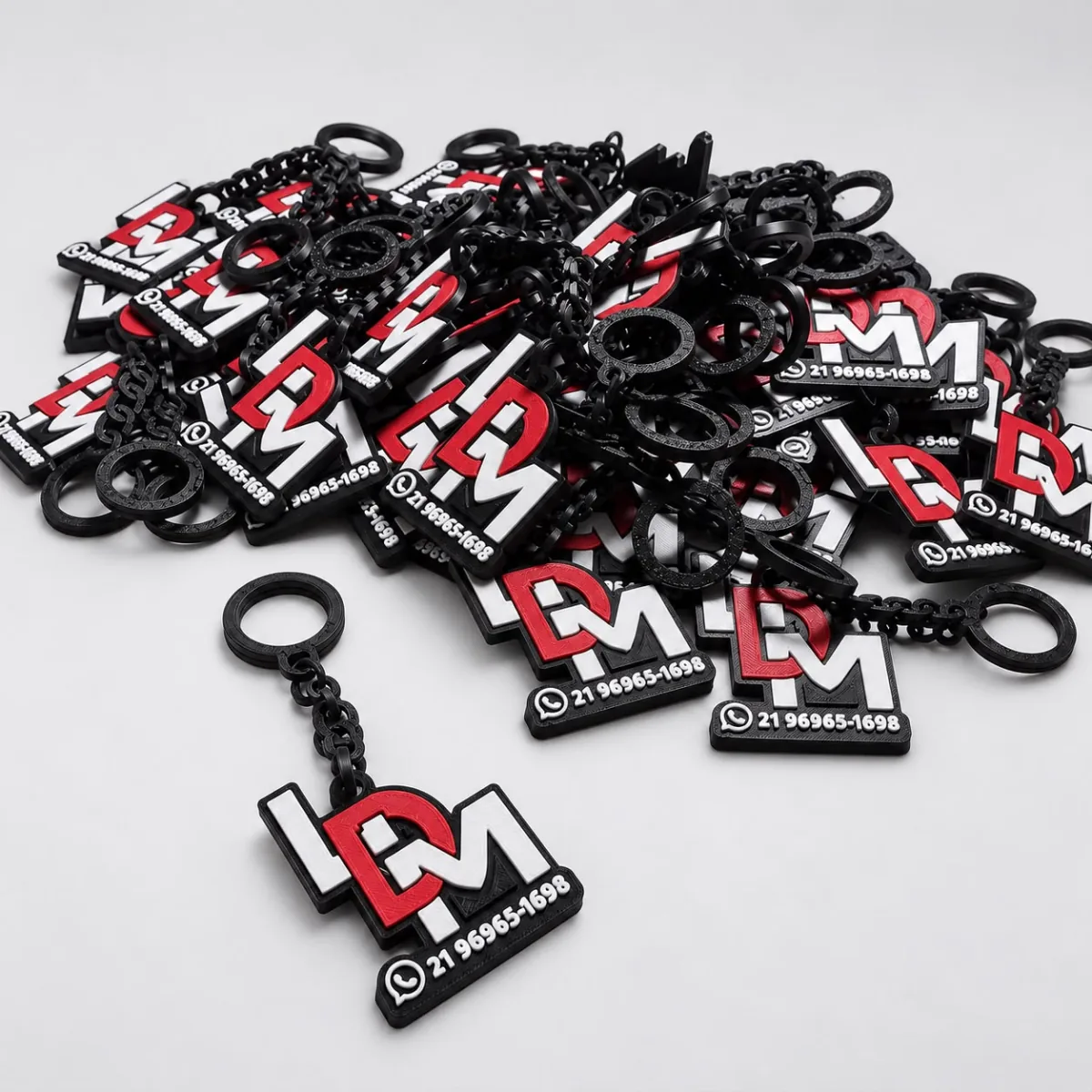 Pilha de chaveiros pretos com o logo de uma empresa em vermelho e branco e o número de WhatsApp